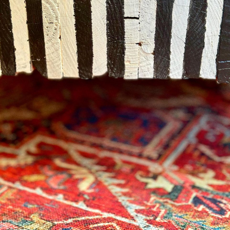 Table basse en bois brut peint à rayures noires et blanches sur un tapis persan rouge